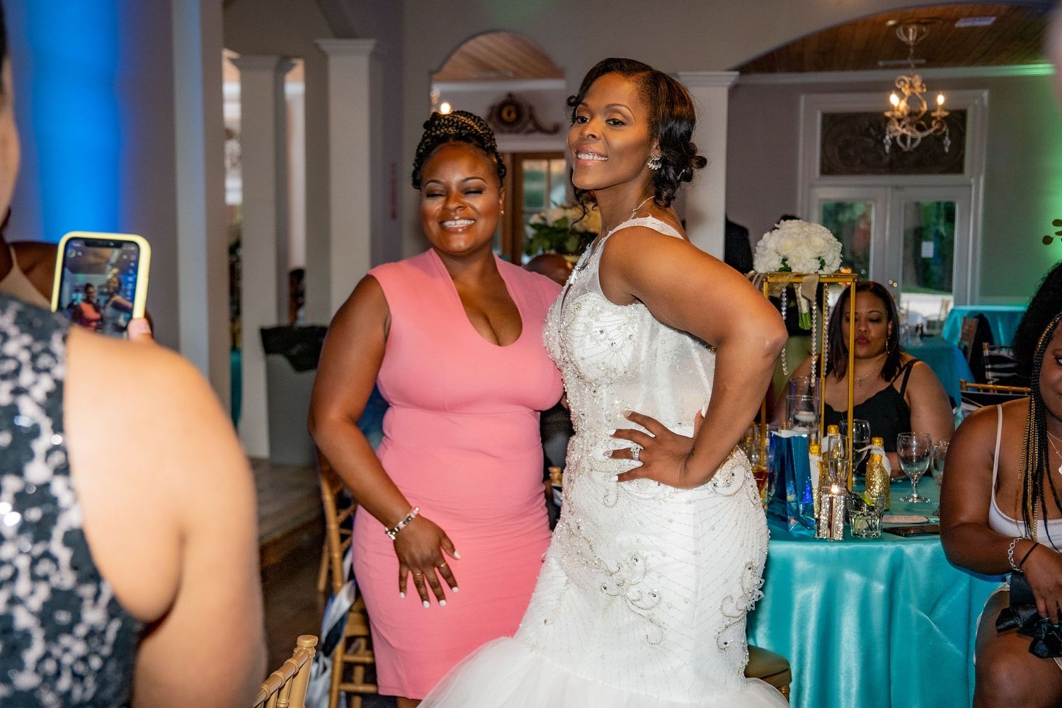 Bride in white mermaid gown poses with guest in pink dress at reception.
