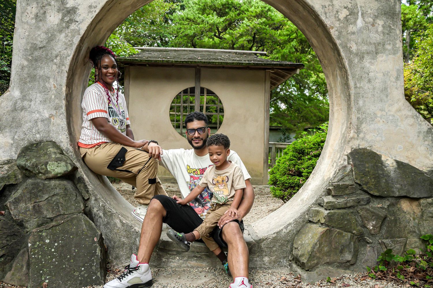 Family of three posing in a circular stone moon gate surrounded by lush greenery in a Japanese garden.