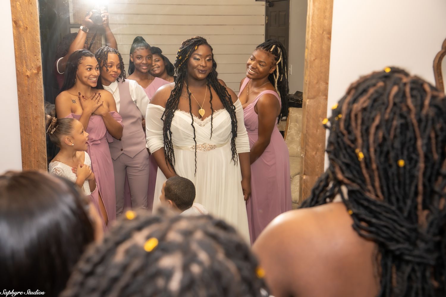 Bride in white gown surrounded by bridesmaids in dusty rose dresses before the wedding ceremony.
