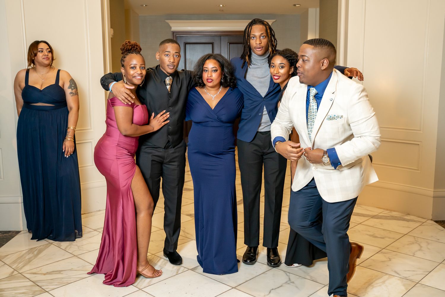Group of elegantly dressed people posing together in formal attire at an indoor event venue.