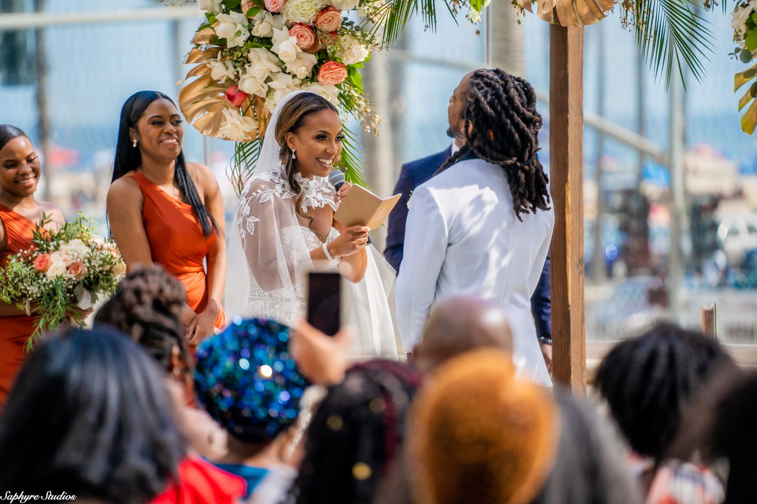 Bride and groom exchange vows under a floral arch at an outdoor wedding ceremony.
