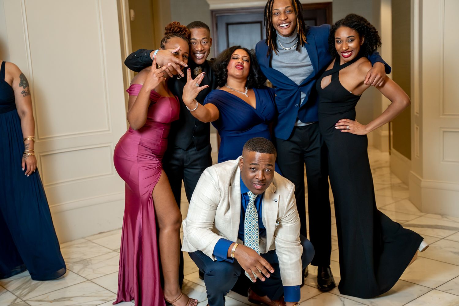 Festive group in formal wear laughing and posing together in a bright indoor hallway.