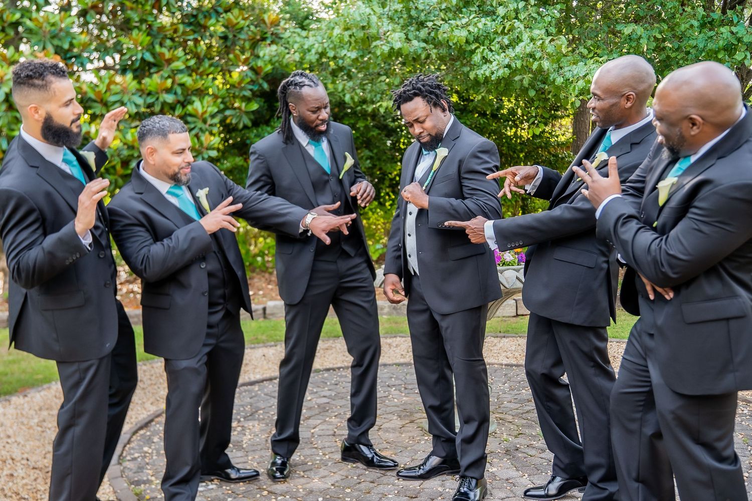 Six groomsmen in black suits with teal accessories pose together outdoors.