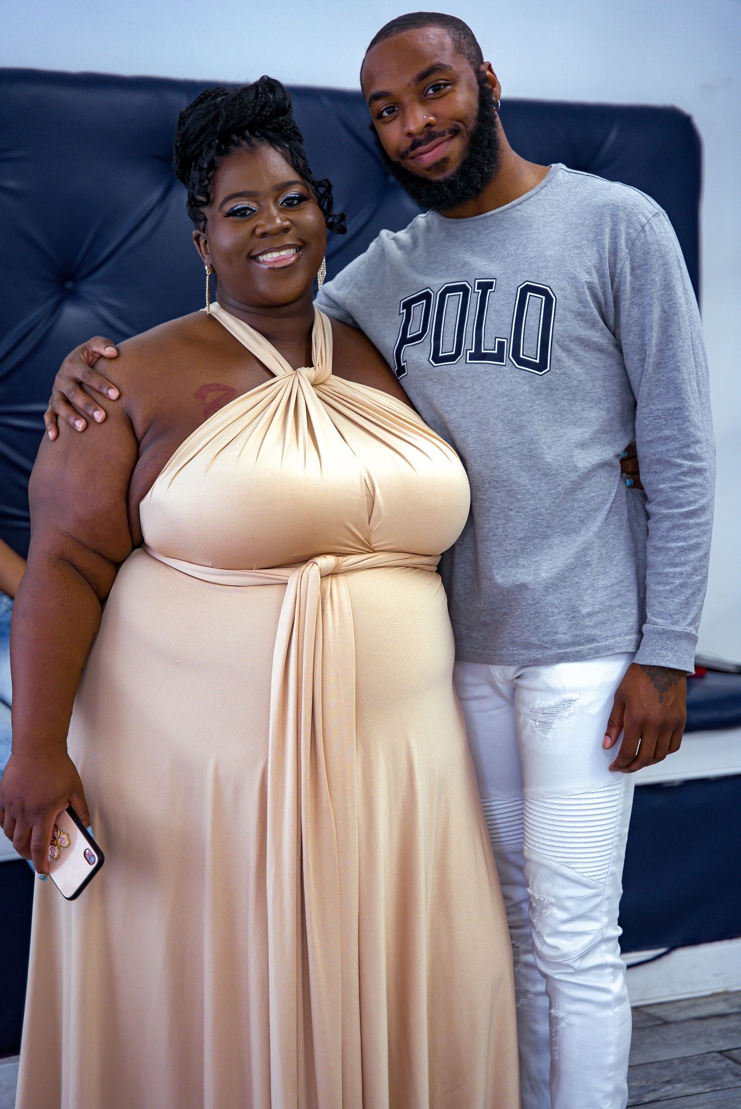 Smiling couple poses together at event, woman in beige halter gown, man in Polo sweatshirt.