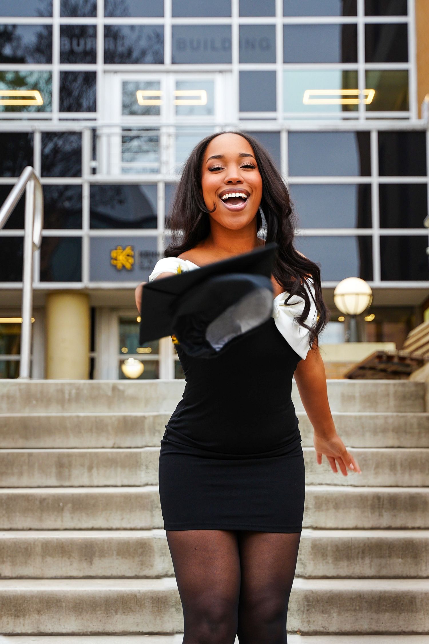 Laughing graduate tosses cap on steps outside Kennesaw State University Nursing Building.