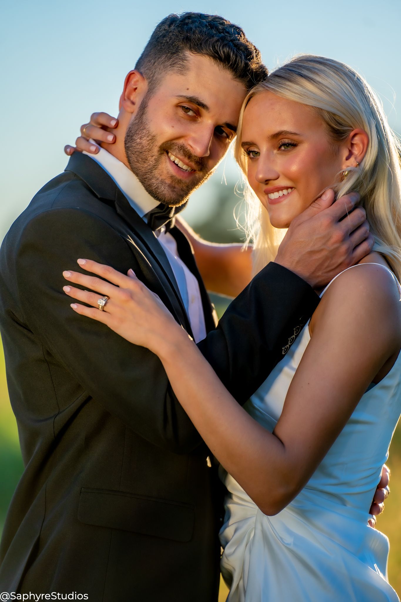 Smiling bride and groom embrace closely outdoors during golden hour wedding portrait photography.
