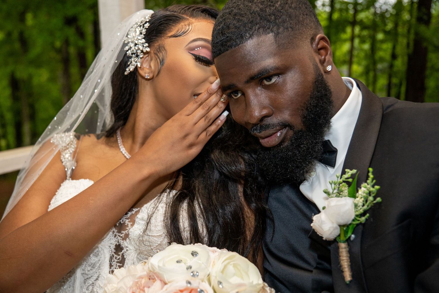 Bride in lace gown whispers to bearded groom during intimate outdoor wedding ceremony.