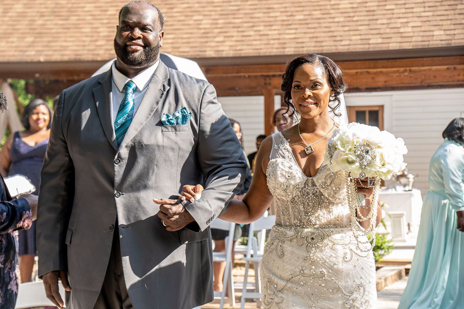 A groom in grey suit and bride in beaded wedding gown walk down the aisle smiling.