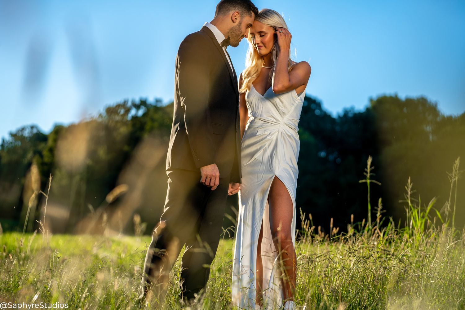 Bride and groom sharing an intimate moment in a sunlit meadow with tall grass.