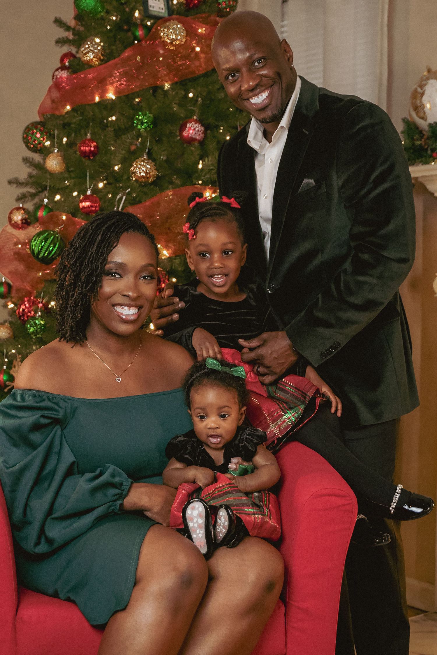 Happy family of four poses in festive holiday attire in front of decorated Christmas tree.