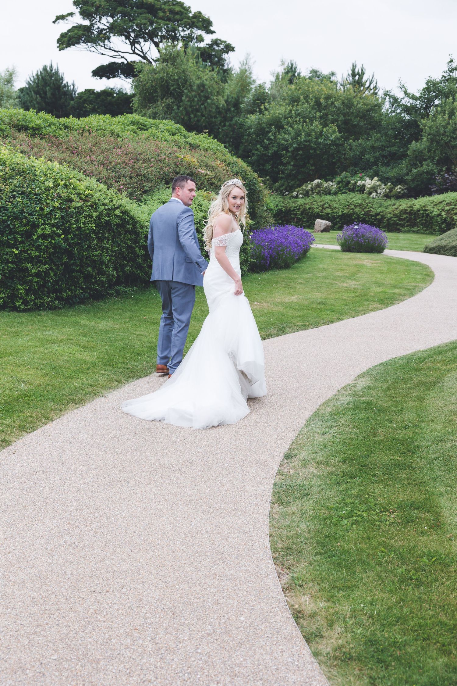 Bride looks back as couple walk path at Seaham Hall; lush gardens and soft, romantic feel.