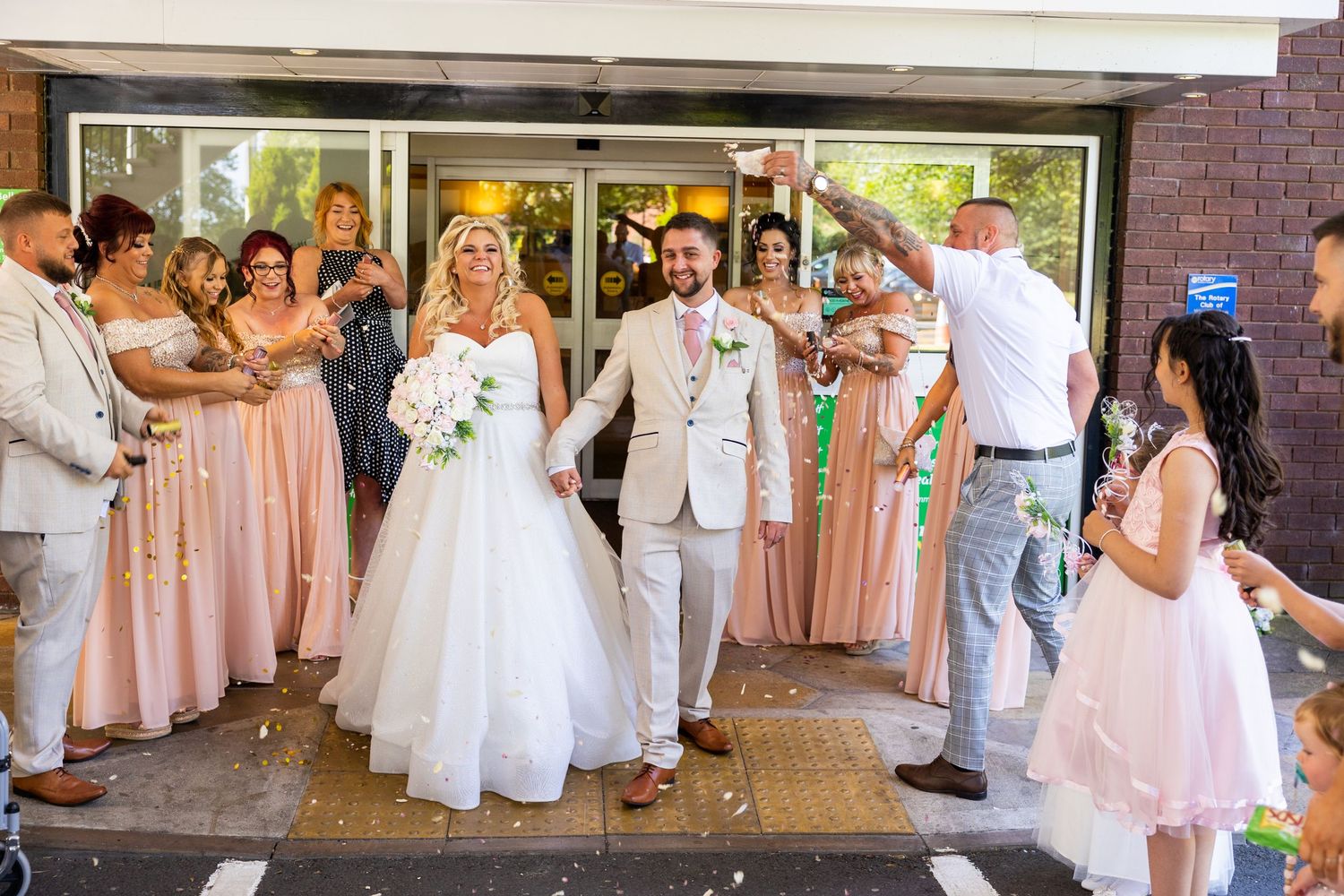 Joyful confetti exit as the newlyweds walk hand in hand, surrounded by cheering family and friends outside the venue.