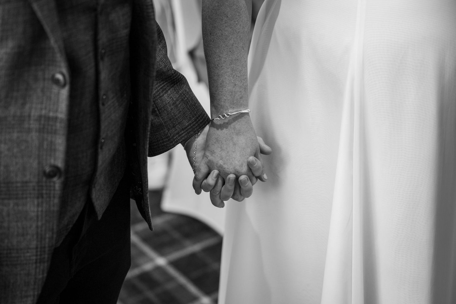 Bride and groom hold hands during ceremony, intimate black and white wedding moment at North East UK venue with timeless romantic feel