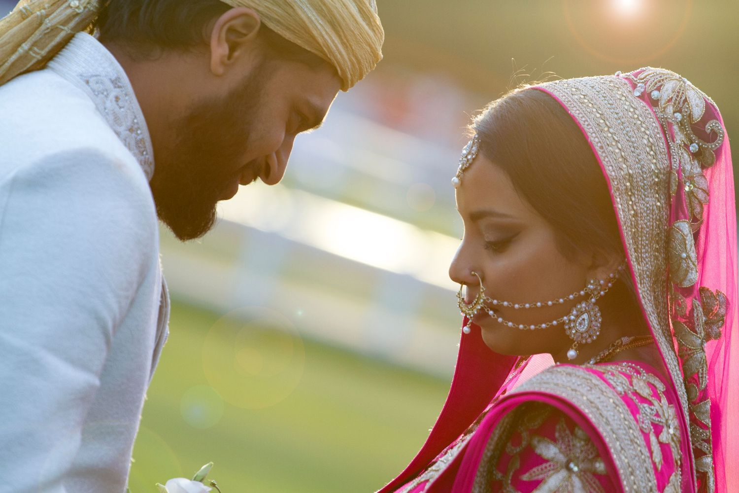 Asian bride and groom in traditional attire at Gosforth Park Racecourse, romantic sunset portrait with elegant cultural details