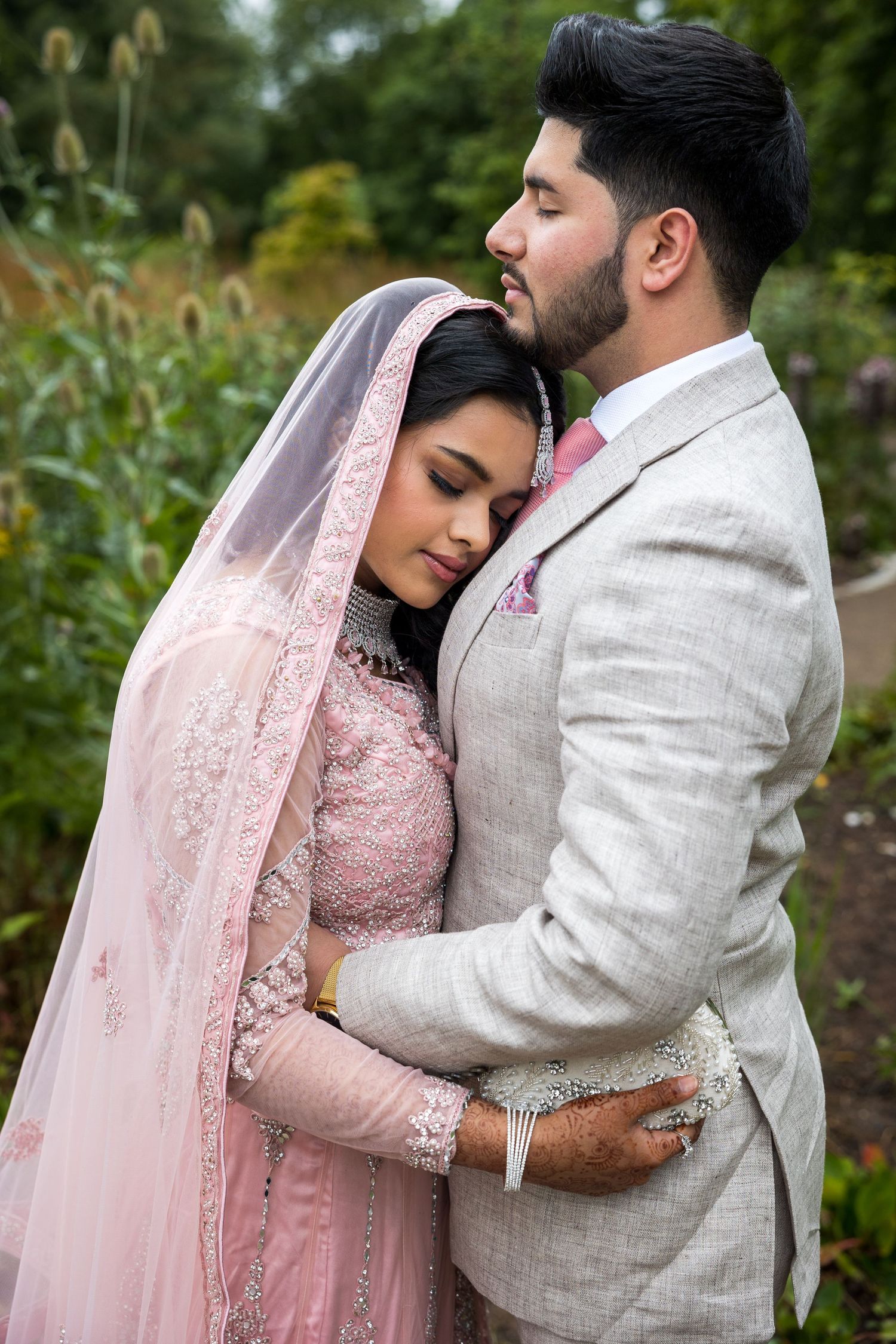 Asian bride and groom embrace outdoors, traditional pink bridal dress, romantic wedding portrait, natural garden setting