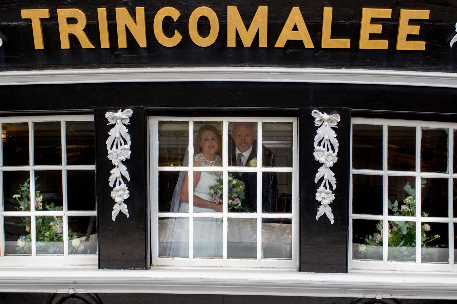 Bride and groom smile through window at Trincomalee wedding venue, a charming North East UK location for elegant weddings and celebrations
