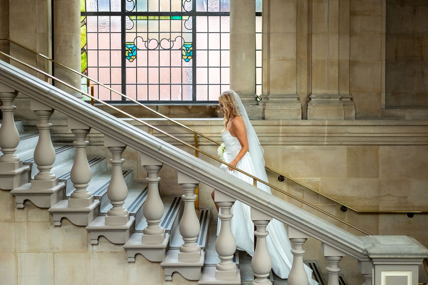 Bride descends staircase at South Shields Registry Office; elegant stone and stained glass backdrop.