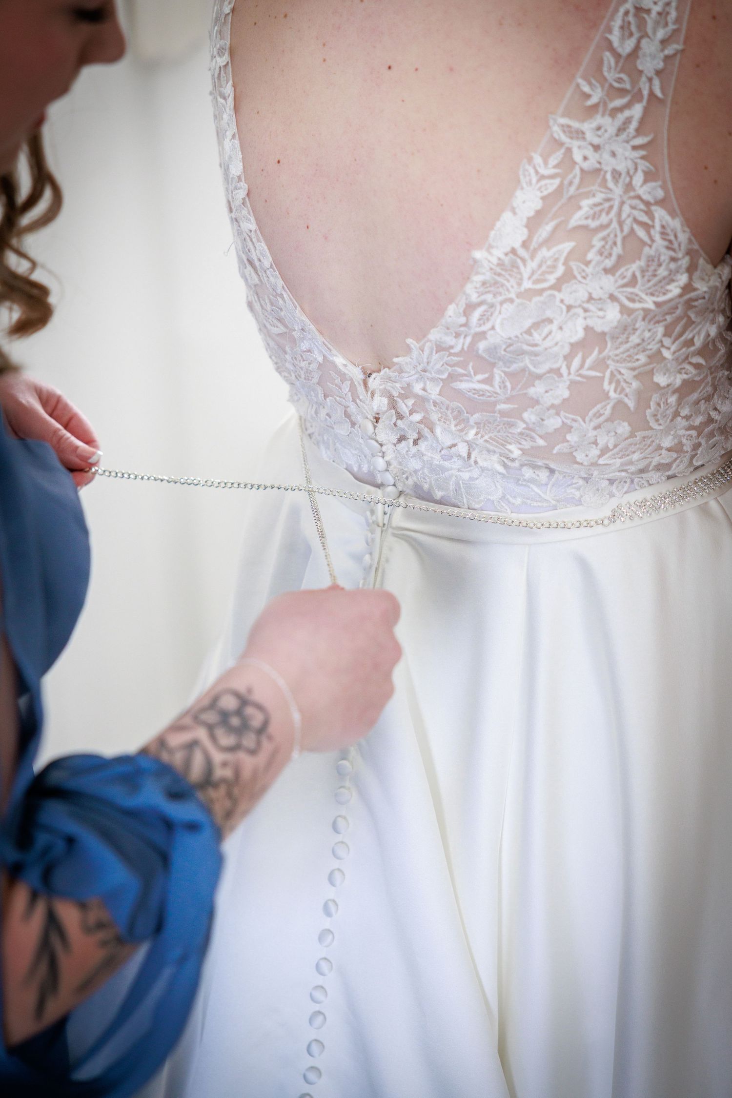 Bridal gown being buttoned at Danby Castle; delicate lace back and careful finishing touches before the ceremony.