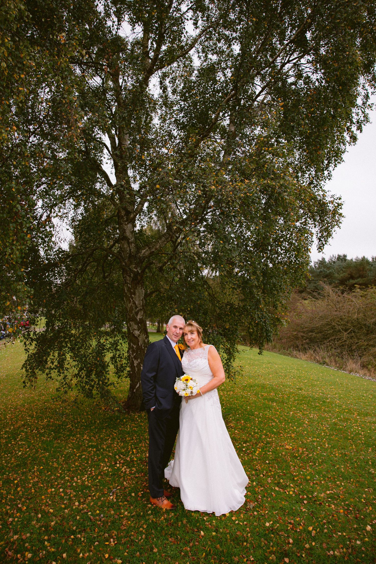 Bride and groom under autumn tree at Beamish Hall, colourful leaves, romantic outdoor wedding portrait, natural countryside setting