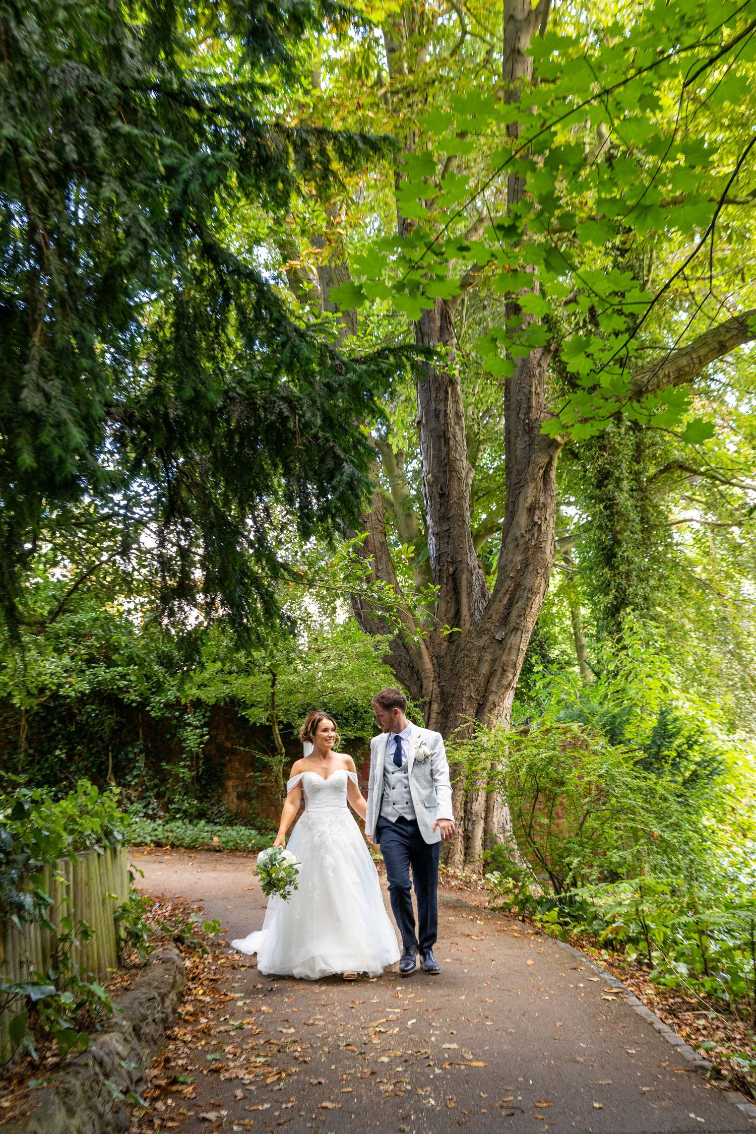 Couple stroll along leafy path, holding hands; peaceful, natural setting with lush greenery.