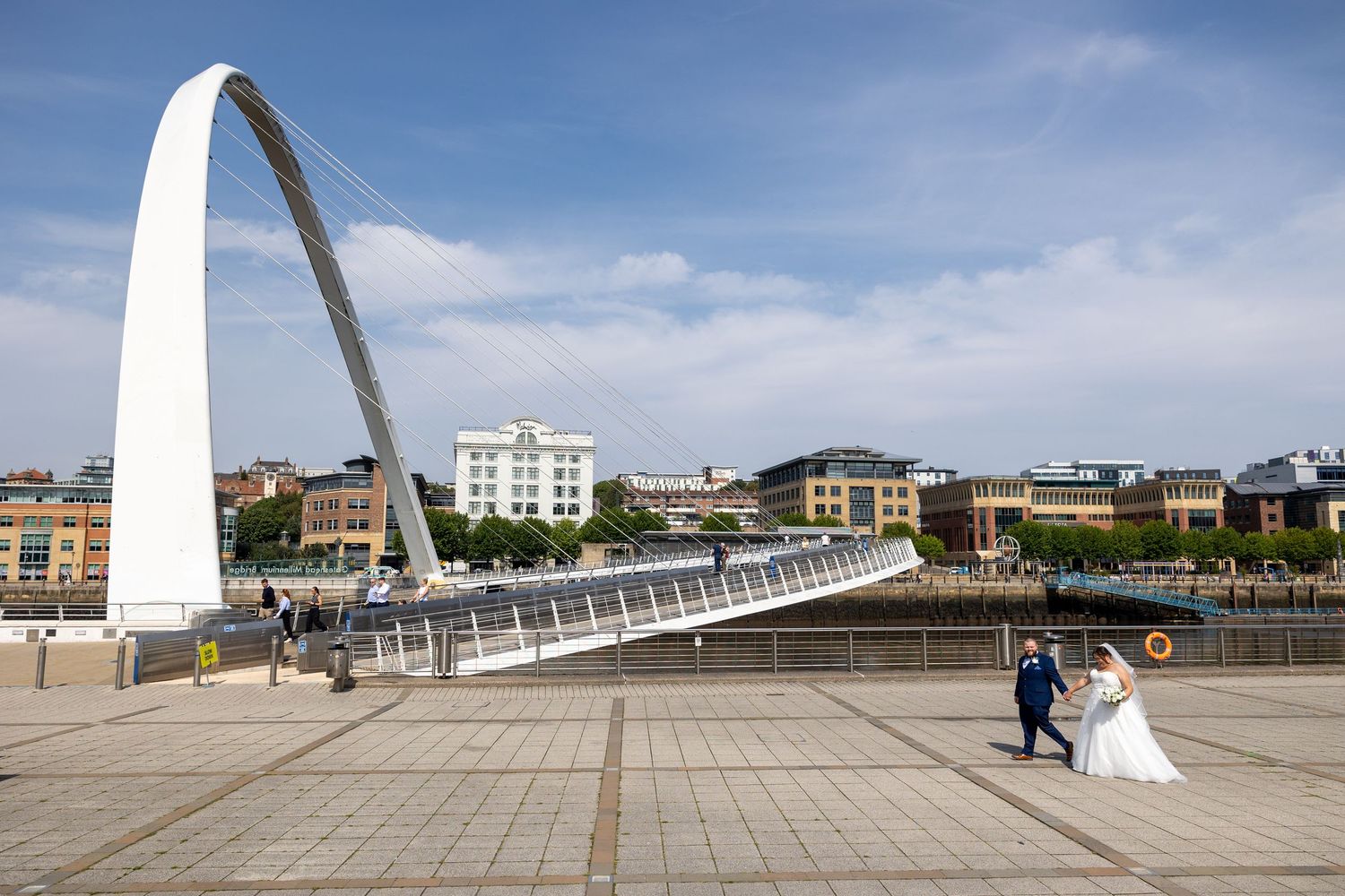 Couple walk by Millennium Bridge, Newcastle; iconic arch frames modern riverside scene.