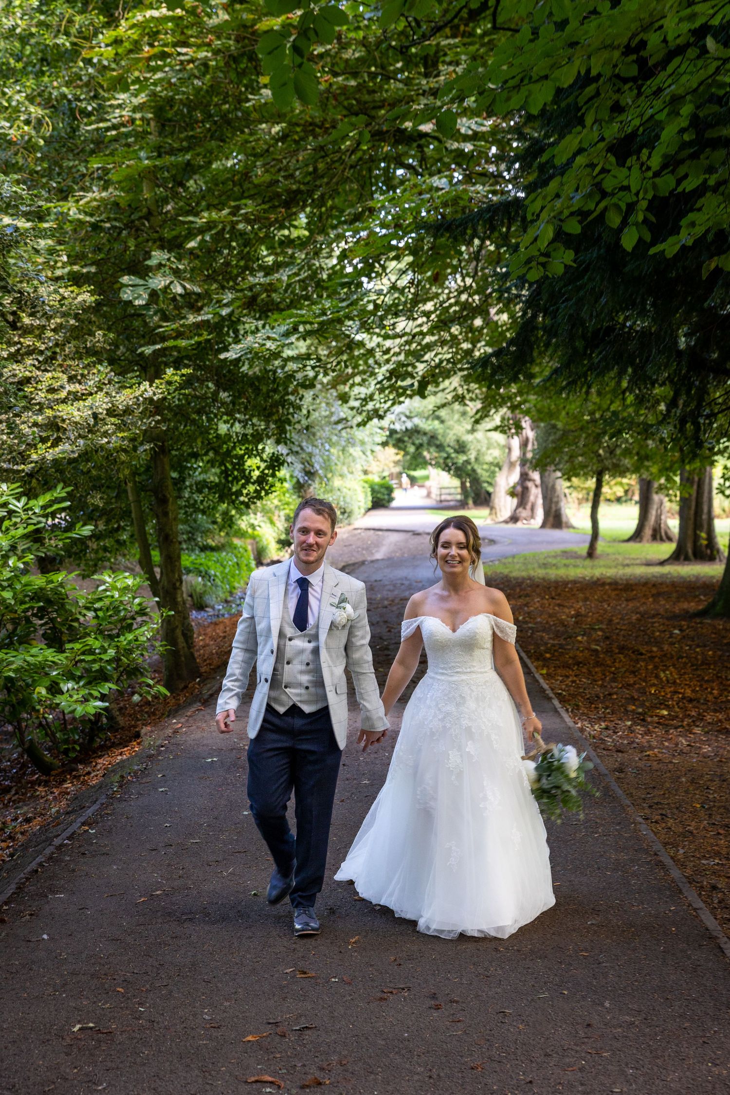 Couple walk hand in hand through tree-lined path; relaxed, joyful moment in natural setting.