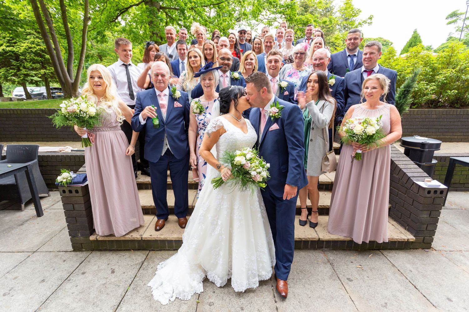 Bride and groom kissing surrounded by wedding guests during group photo at Holiday Inn Washington
