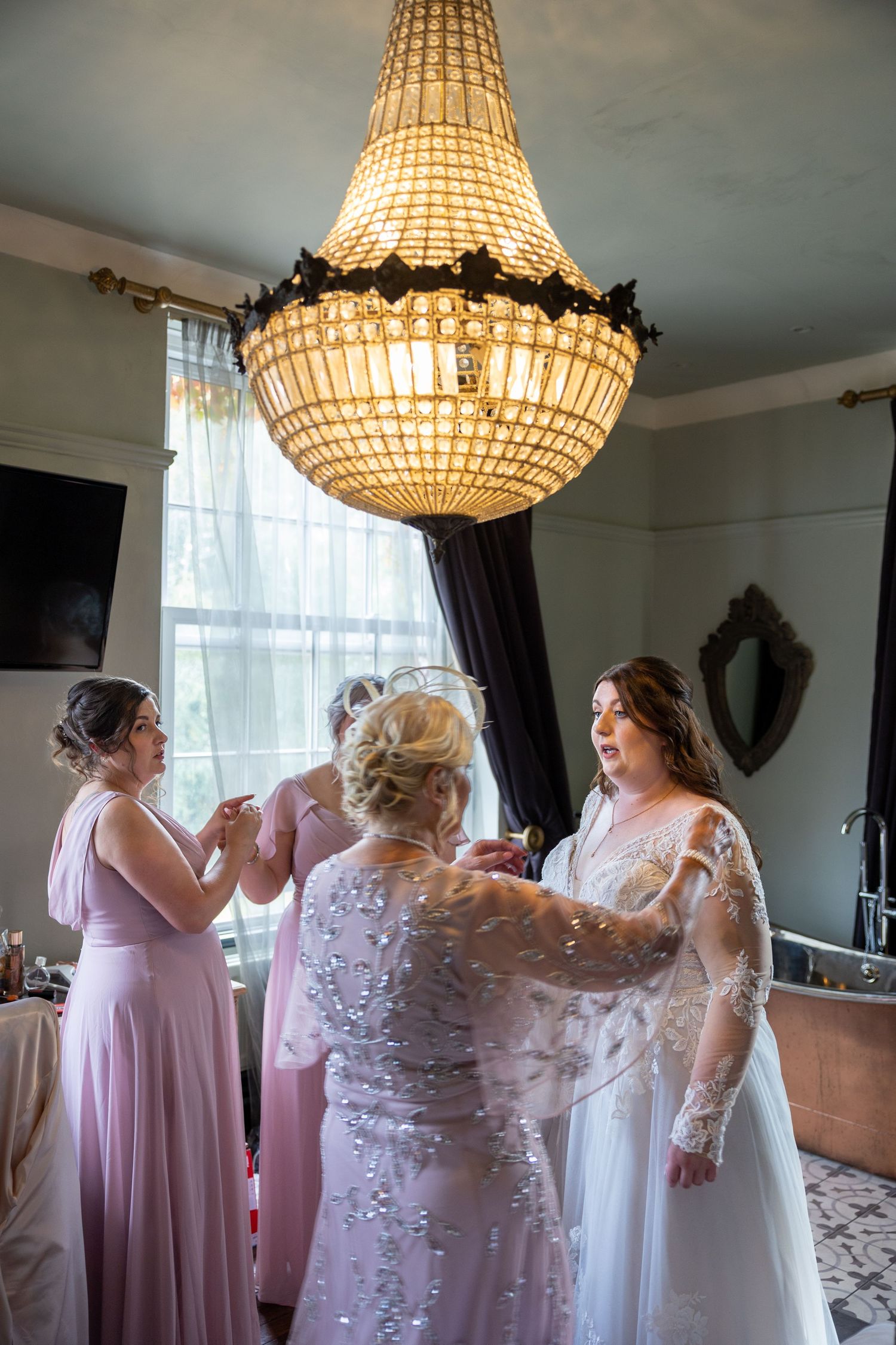 Bridal prep at Bowburn Hall; emotional moment as dress is adjusted beneath grand chandelier.