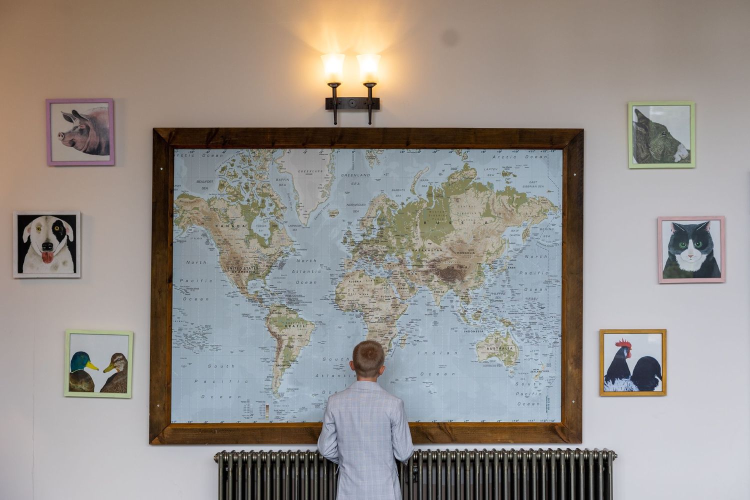 Child stands before world map at South Causey Inn; playful, curious moment with colorful wall art.