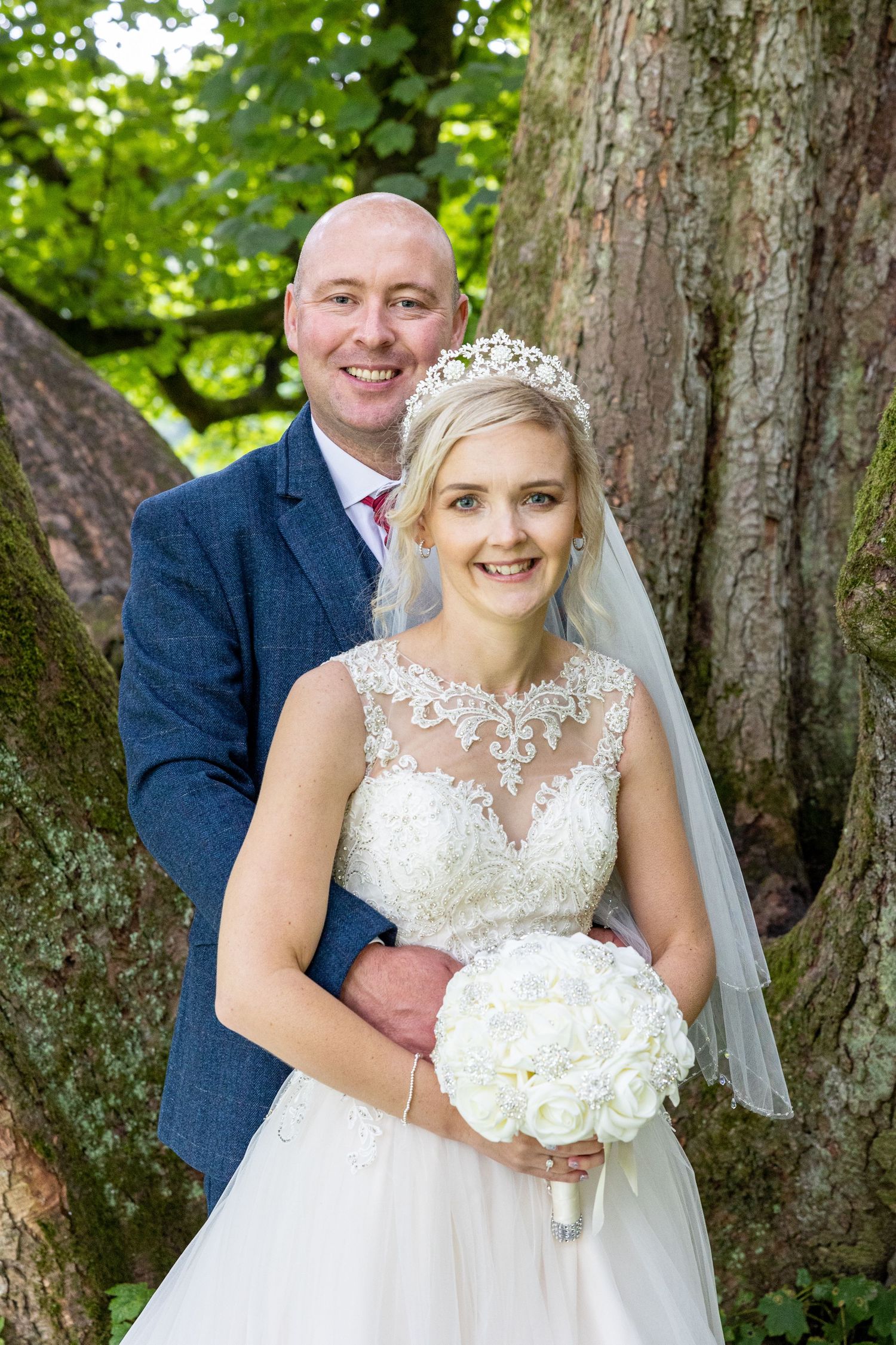 Bride and groom share a romantic moment beneath trees at Redworth Hall, with soft natural light creating a timeless outdoor wedding portrait