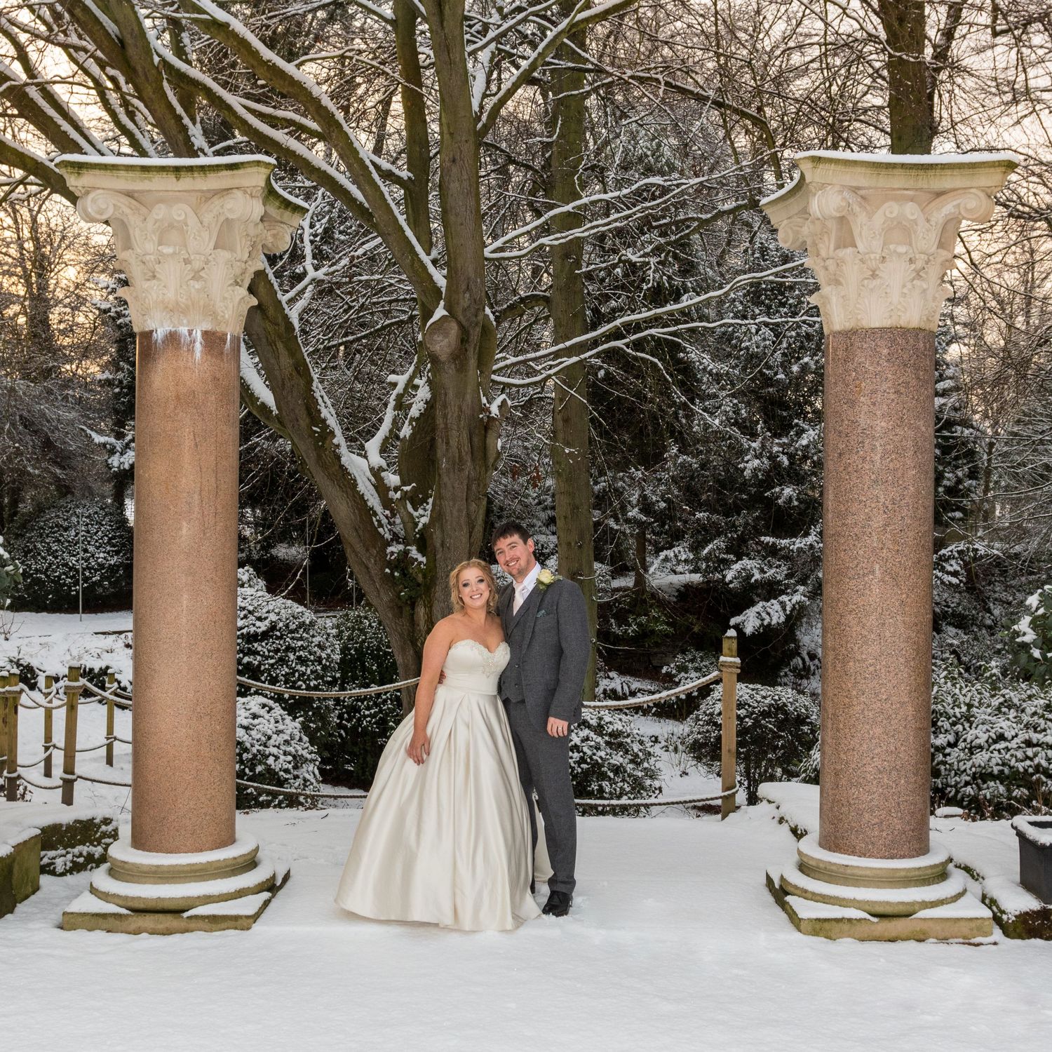 Couple pose between columns at Whitworth Hall; snowy setting creates a magical winter wedding scene.