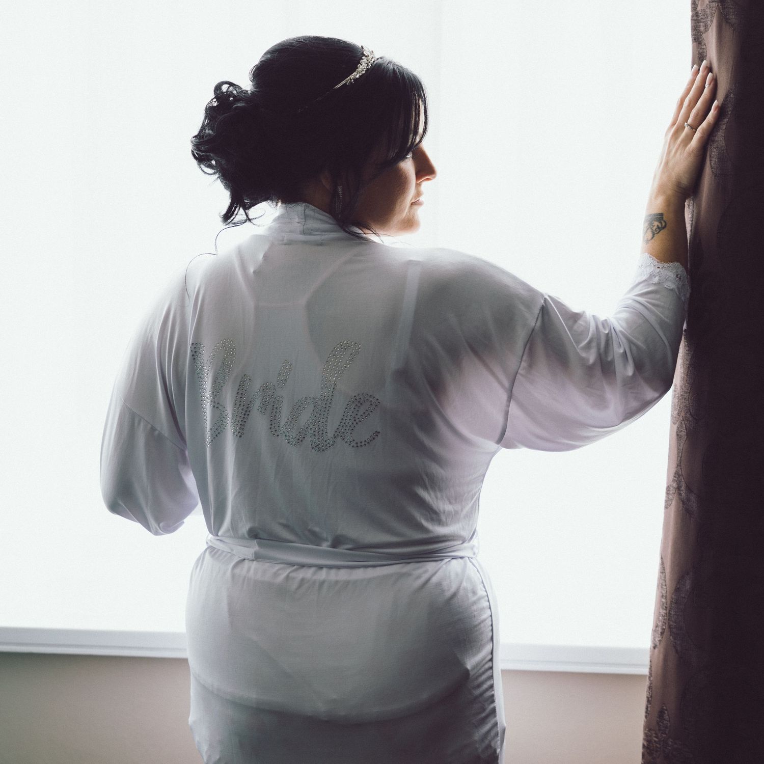 Bride against a window looking side ways while enjoying a drink