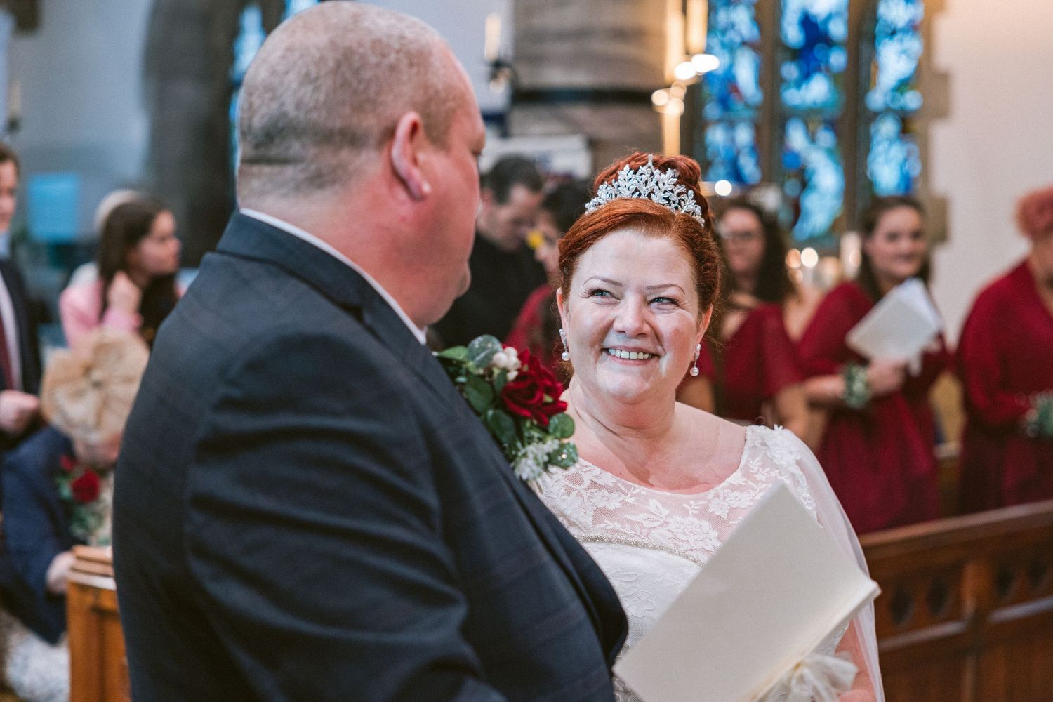 Bride smiles at groom during church ceremony, emotional North East UK wedding moment with guests and warm, romantic atmosphere