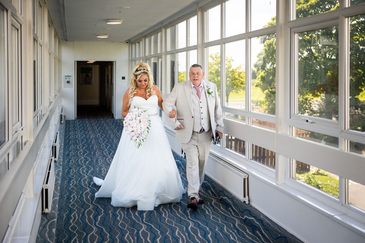 Bride walking down a bright hallway with her father, a quiet, emotional moment just before the ceremony.