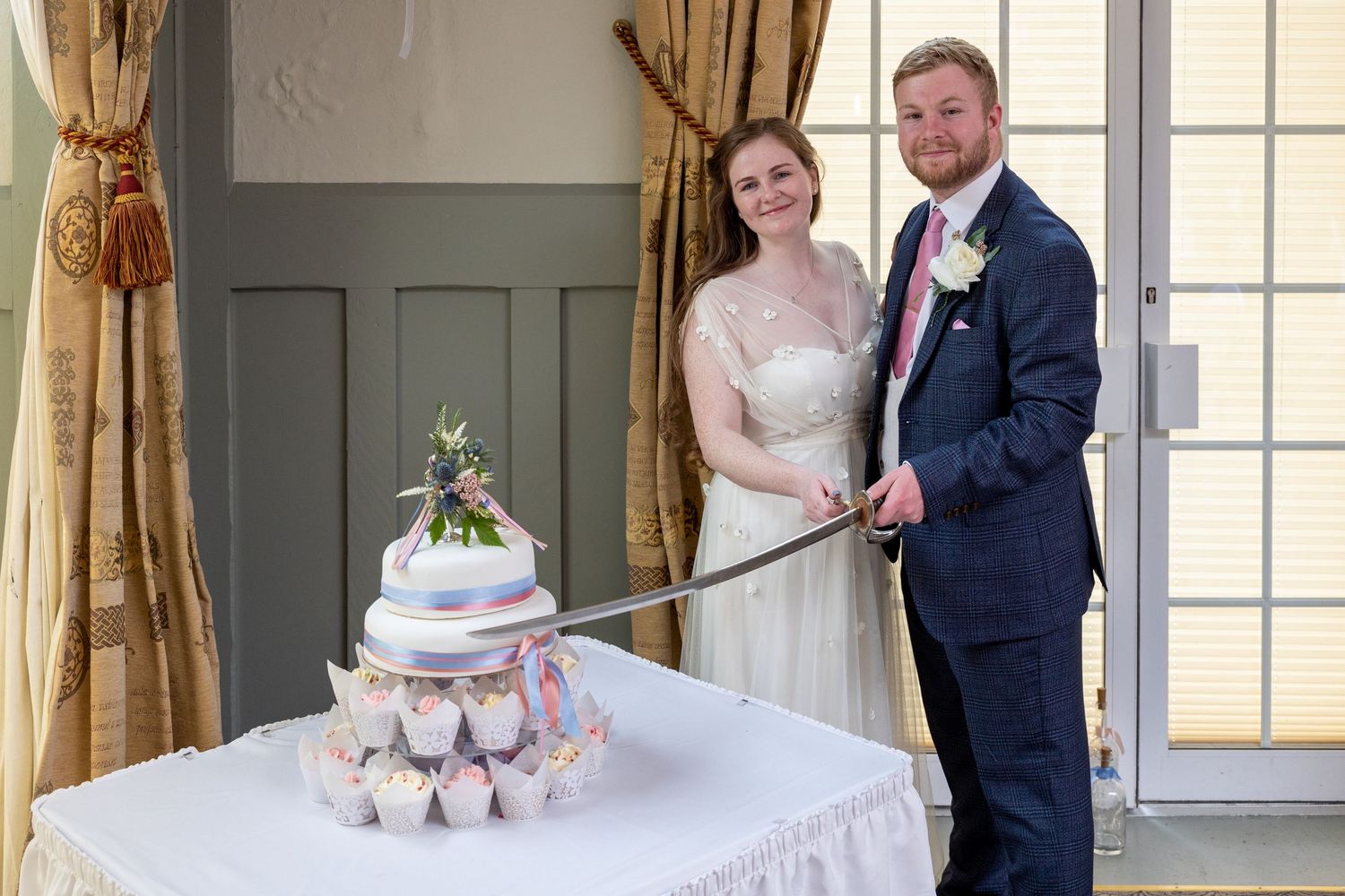 Bride and groom cut wedding cake with sword, unique North East UK wedding moment with elegant setting and traditional celebration style