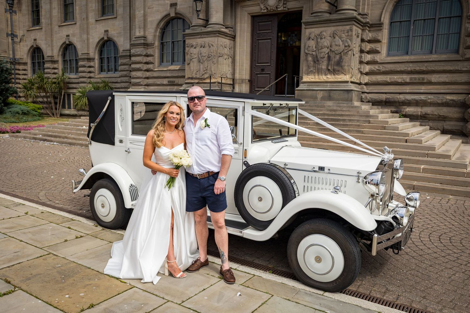 Couple pose by vintage car at South Shields Registry Office; classic setting with historic building backdrop.