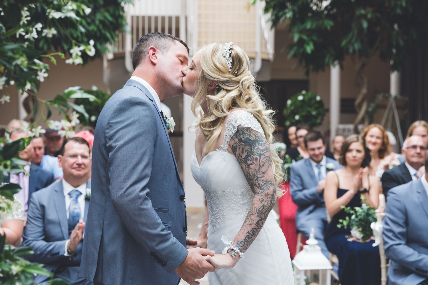 Bride and groom share their first kiss at Seaham Hall wedding ceremony, surrounded by guests in a romantic indoor setting.