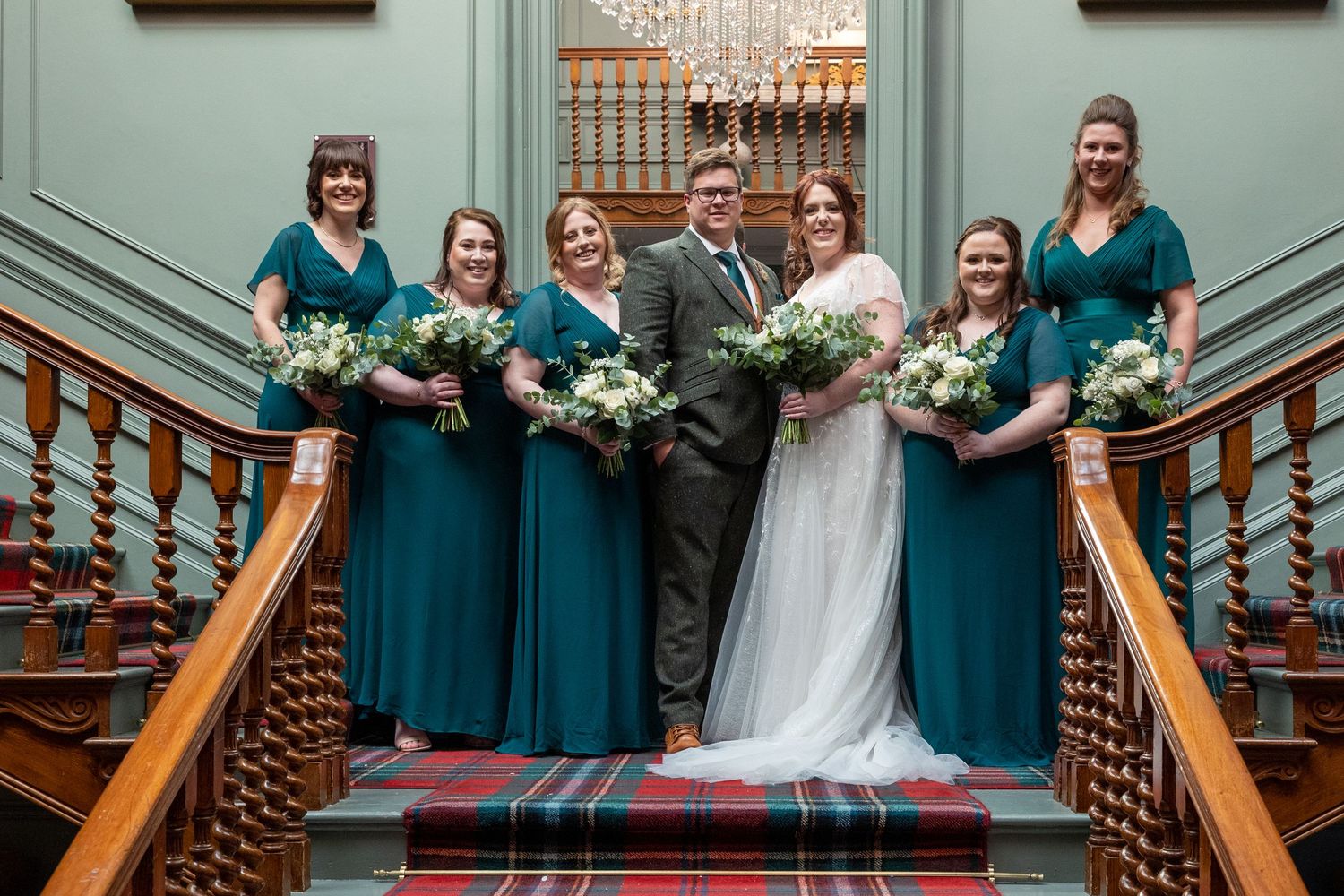 Wedding party on staircase; bride, groom, and bridesmaids pose with bouquets in elegant setting.