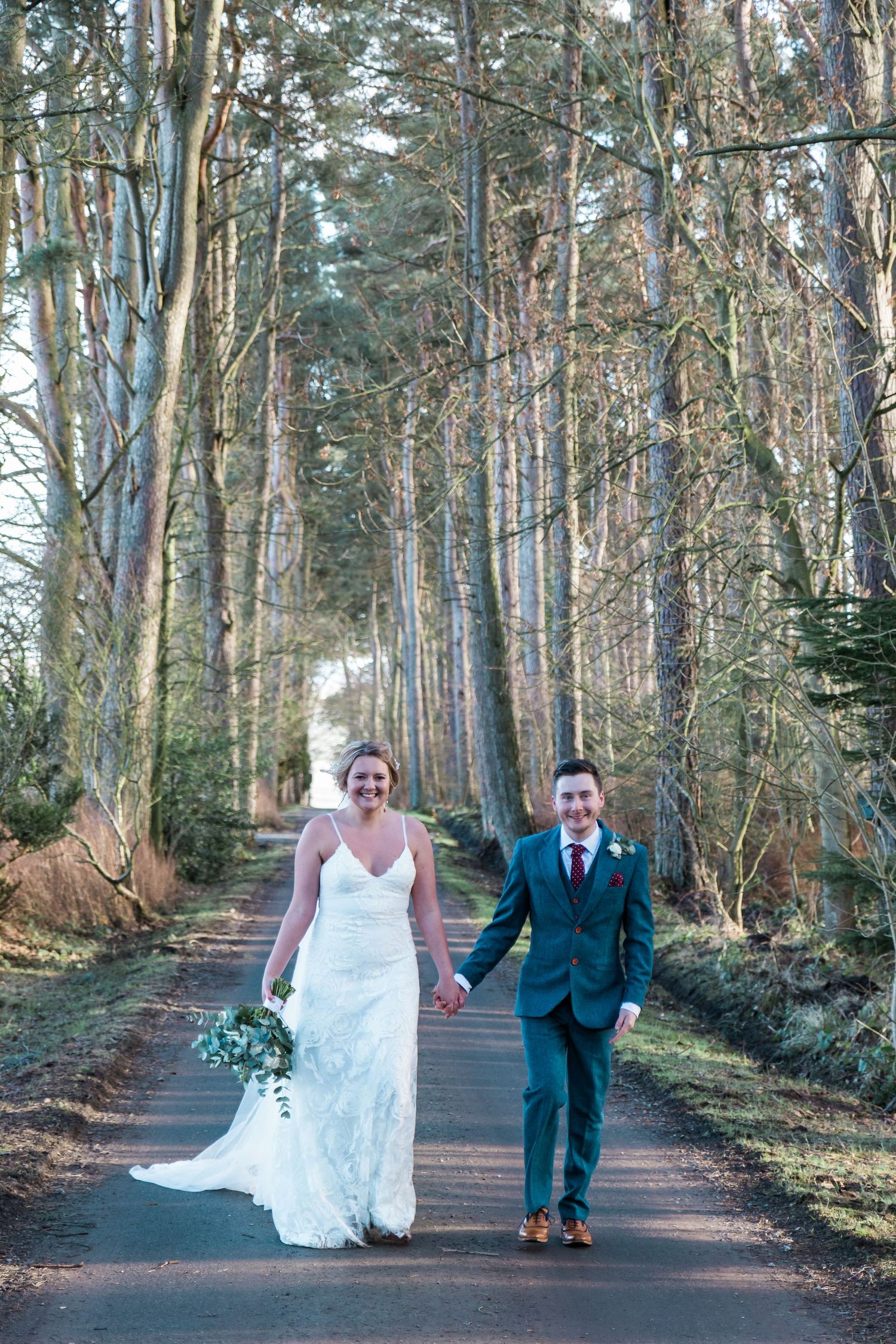 Bride and groom walk through woodland in winter, romantic North East UK wedding photo with natural light and scenic forest backdrop