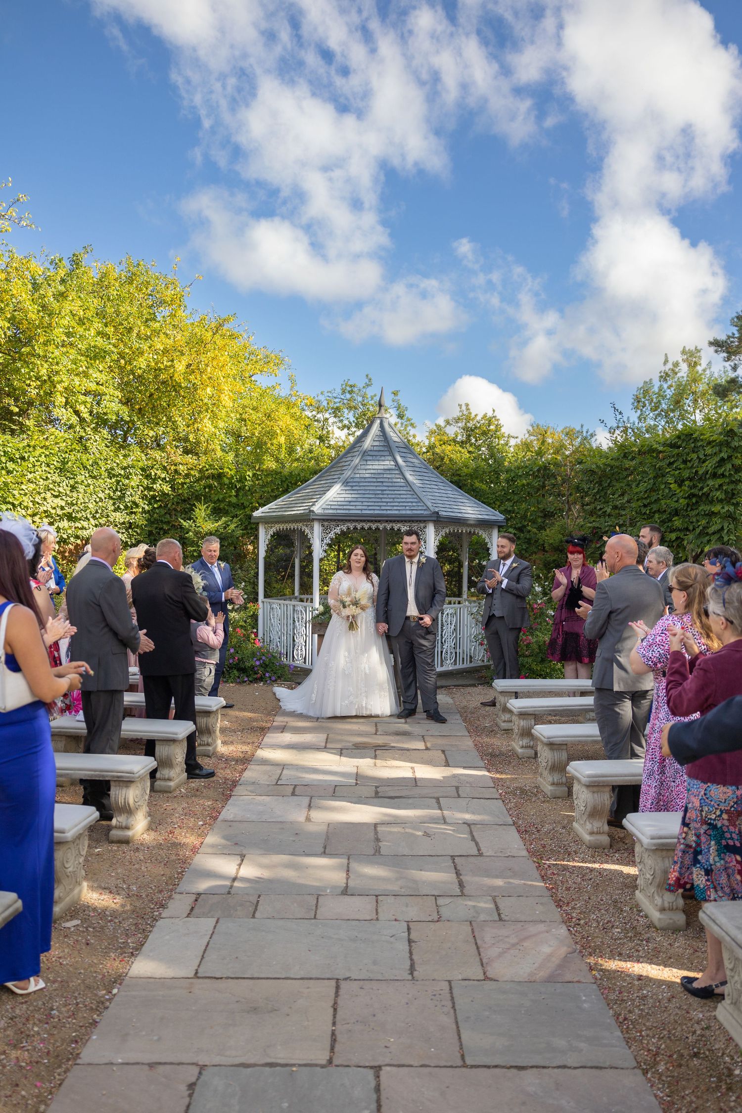 Bride and groom exit gazebo at Bowburn Hall; guests line the aisle under sunny skies.