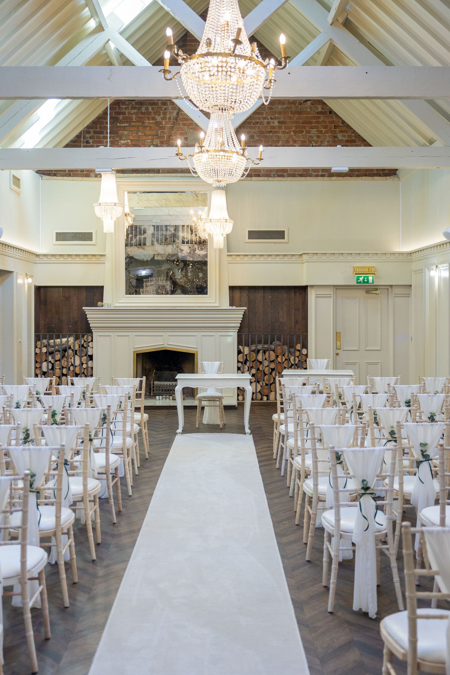 Ceremony setup at Escomb; elegant aisle with chandeliers, fireplace, and soft neutral décor.