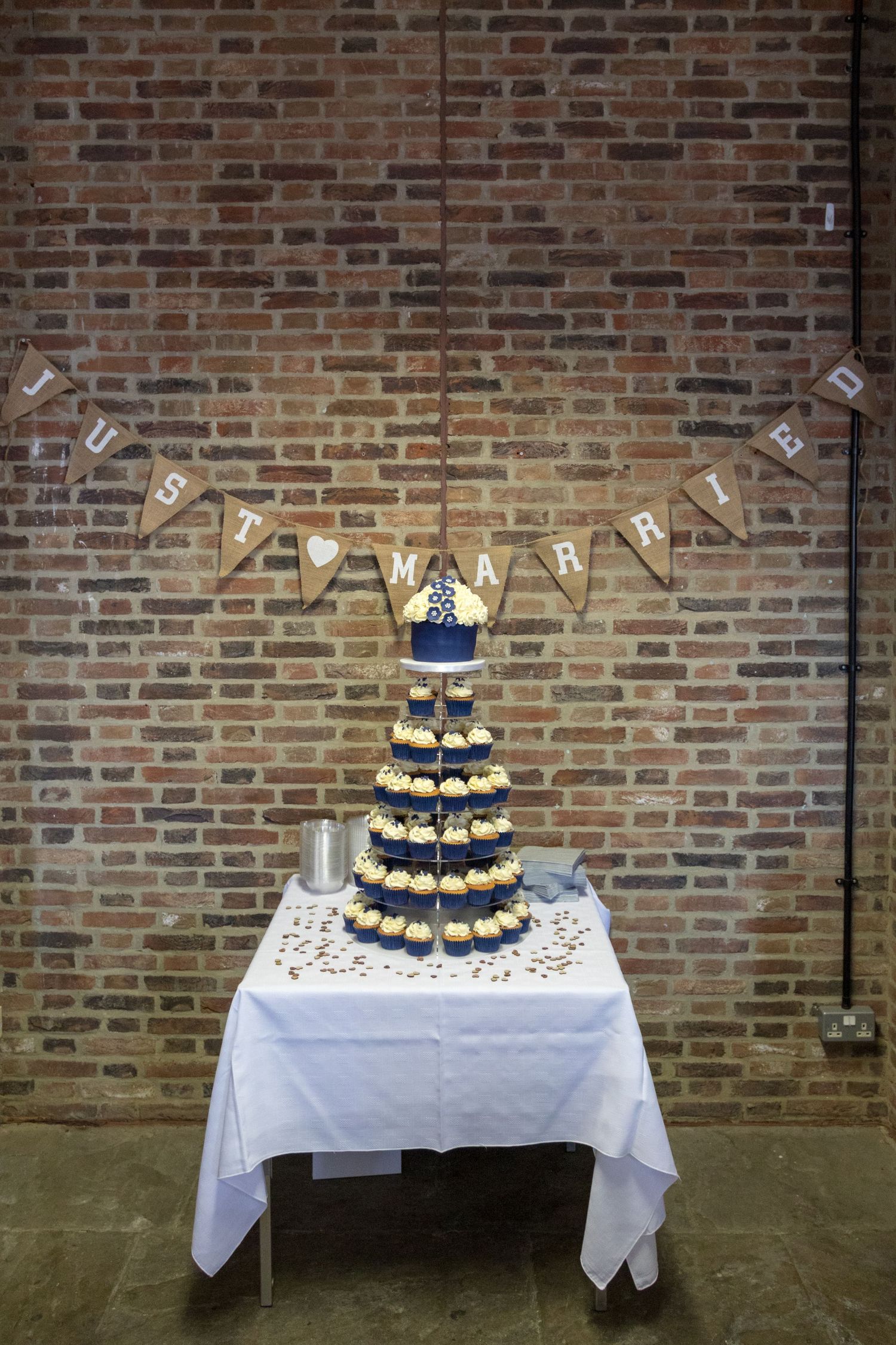 Rustic wedding cupcake tower display with ‘Just Married’ bunting against a brick wall