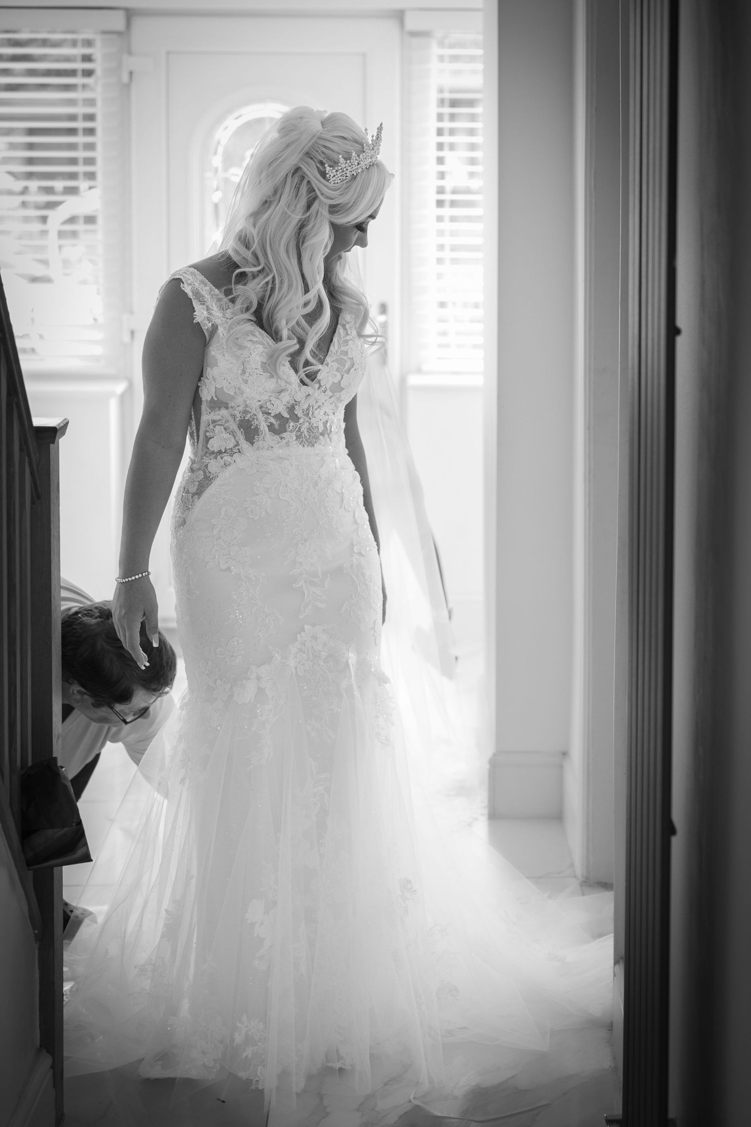 Bride prepares in soft window light as her dress is adjusted, capturing a calm, intimate wedding moment with elegance and anticipation.