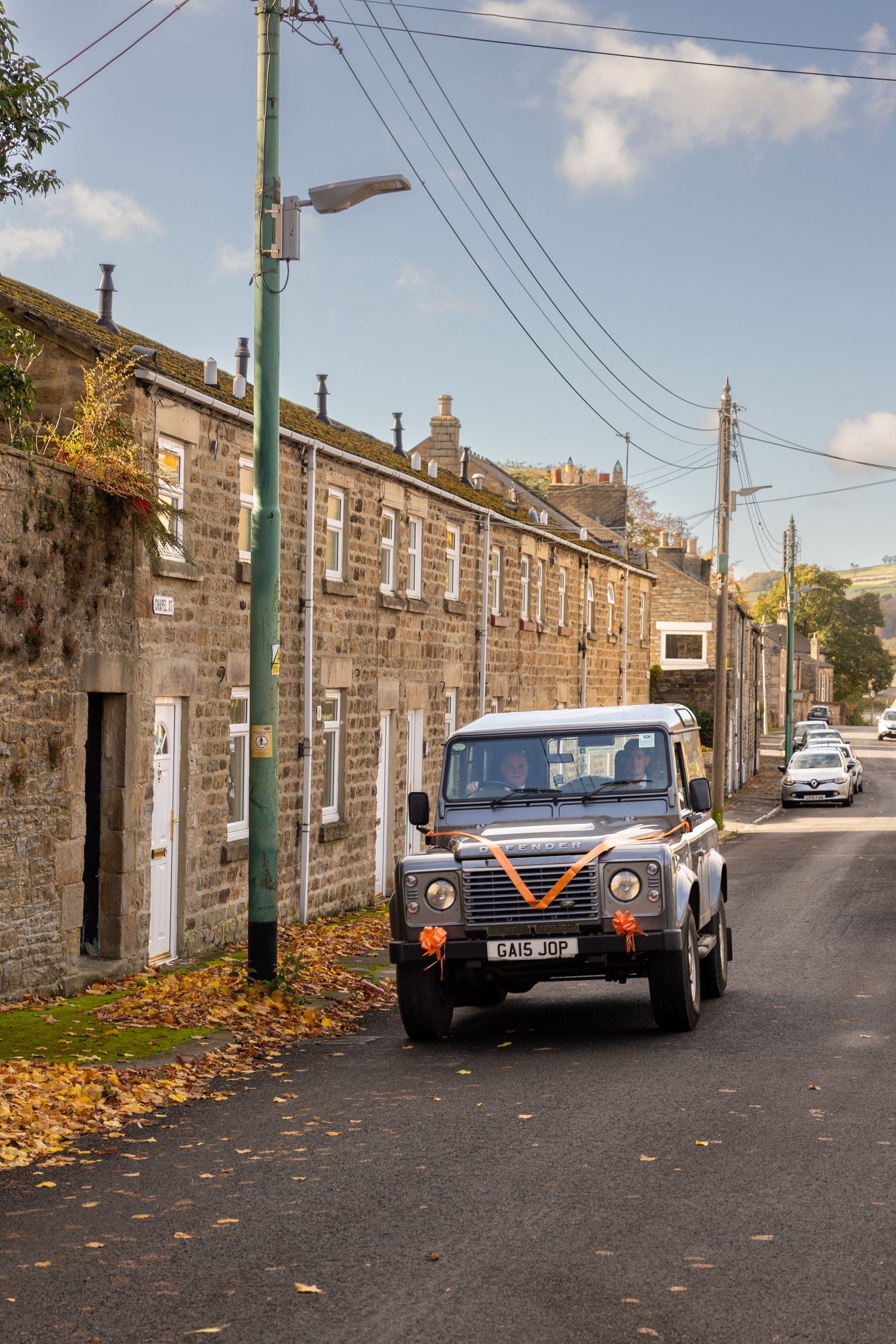 Wedding car arriving in Wolsingham, with a decorated Land Rover Defender driving through the charming village streets.