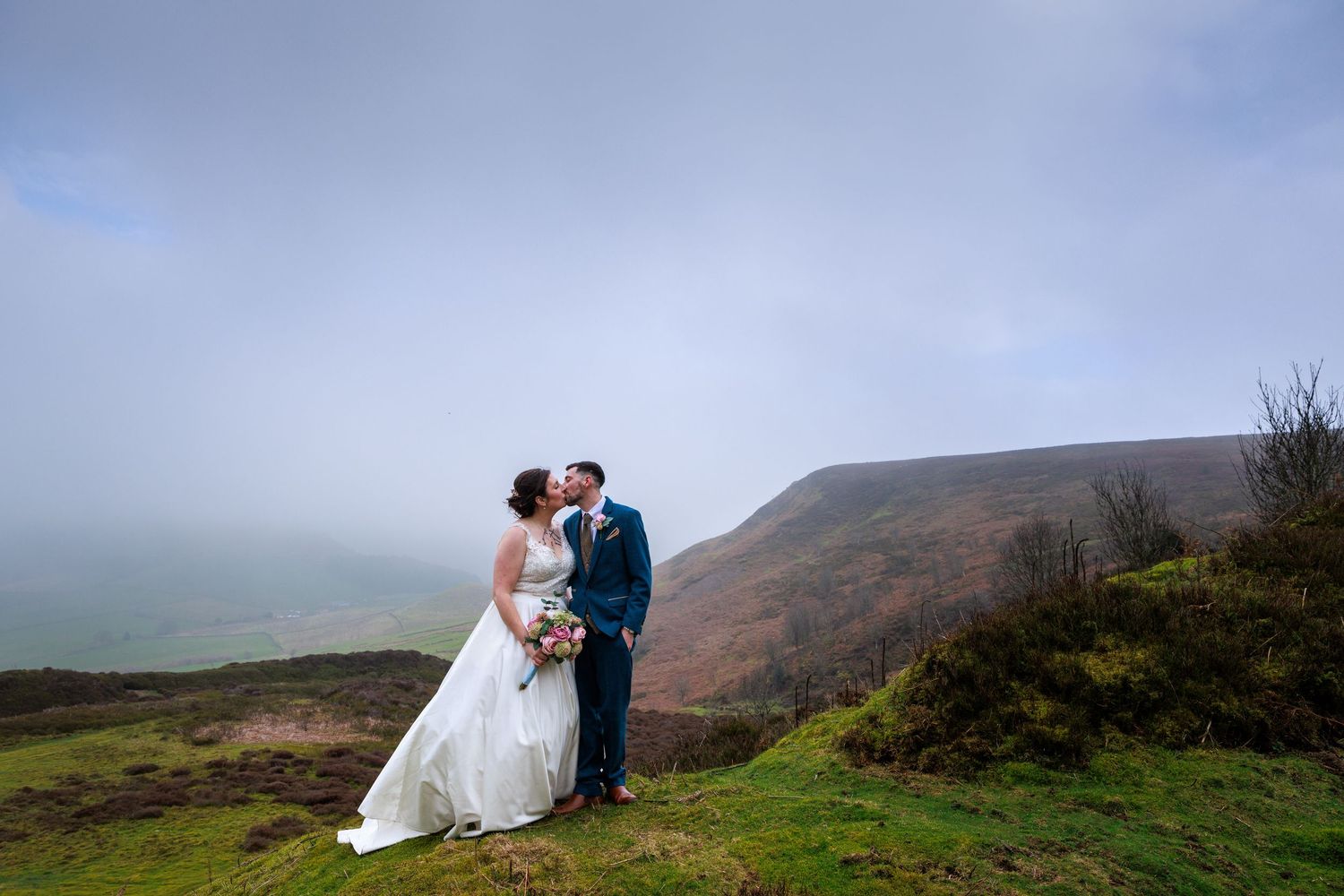 Couple embrace on misty hillside at Danby Castle; Yorkshire Moors create a dramatic, romantic backdrop.