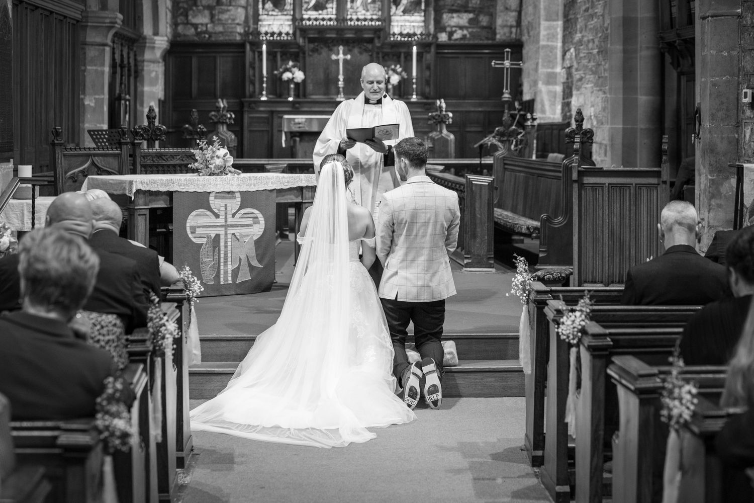 Black and white church wedding ceremony, bride and groom kneeling at altar, emotional vows, classic UK wedding moment, timeless romance