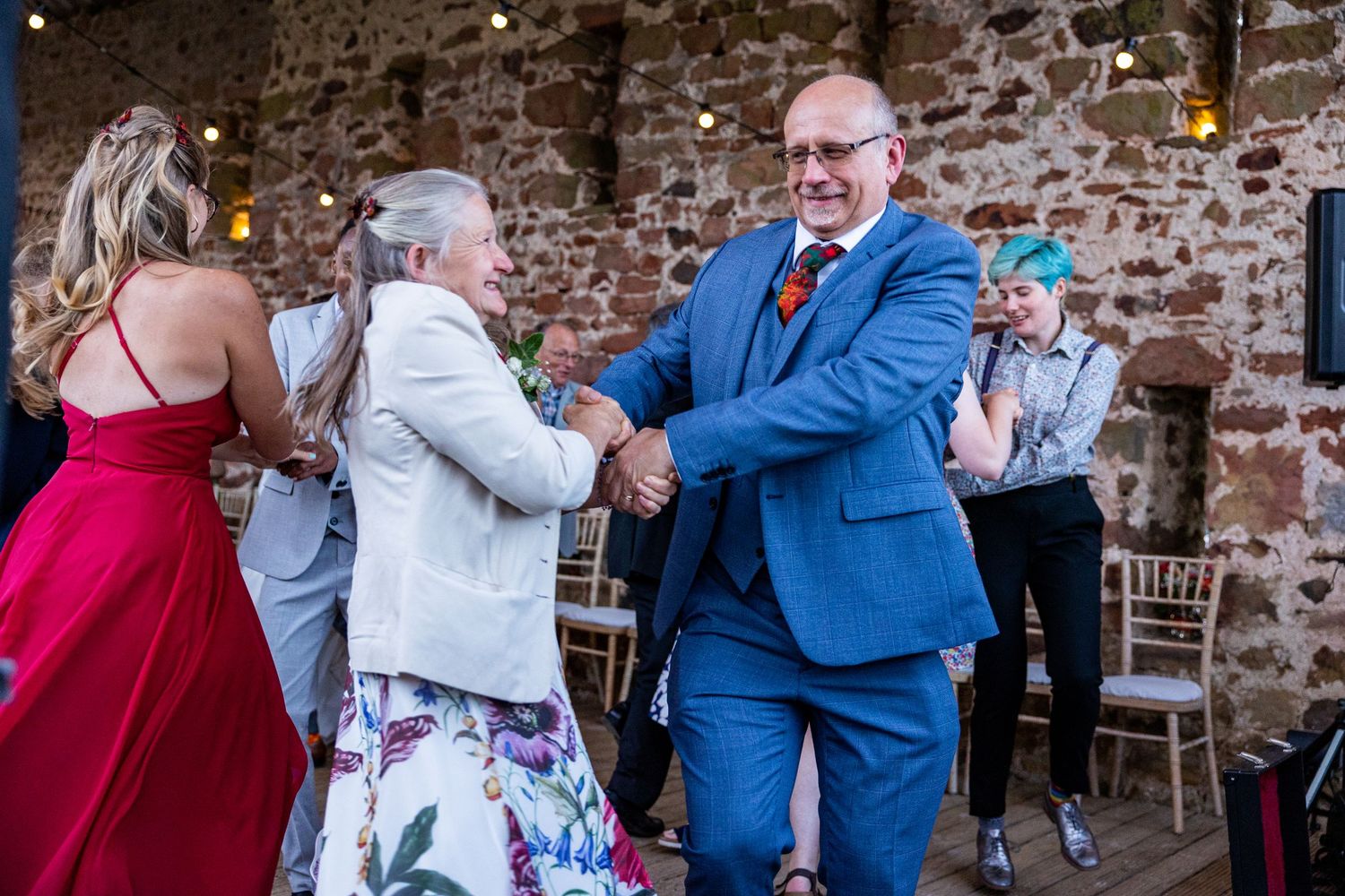 Guests dancing at wedding reception, joyful celebration in rustic barn venue with fairy lights, lively party atmosphere.