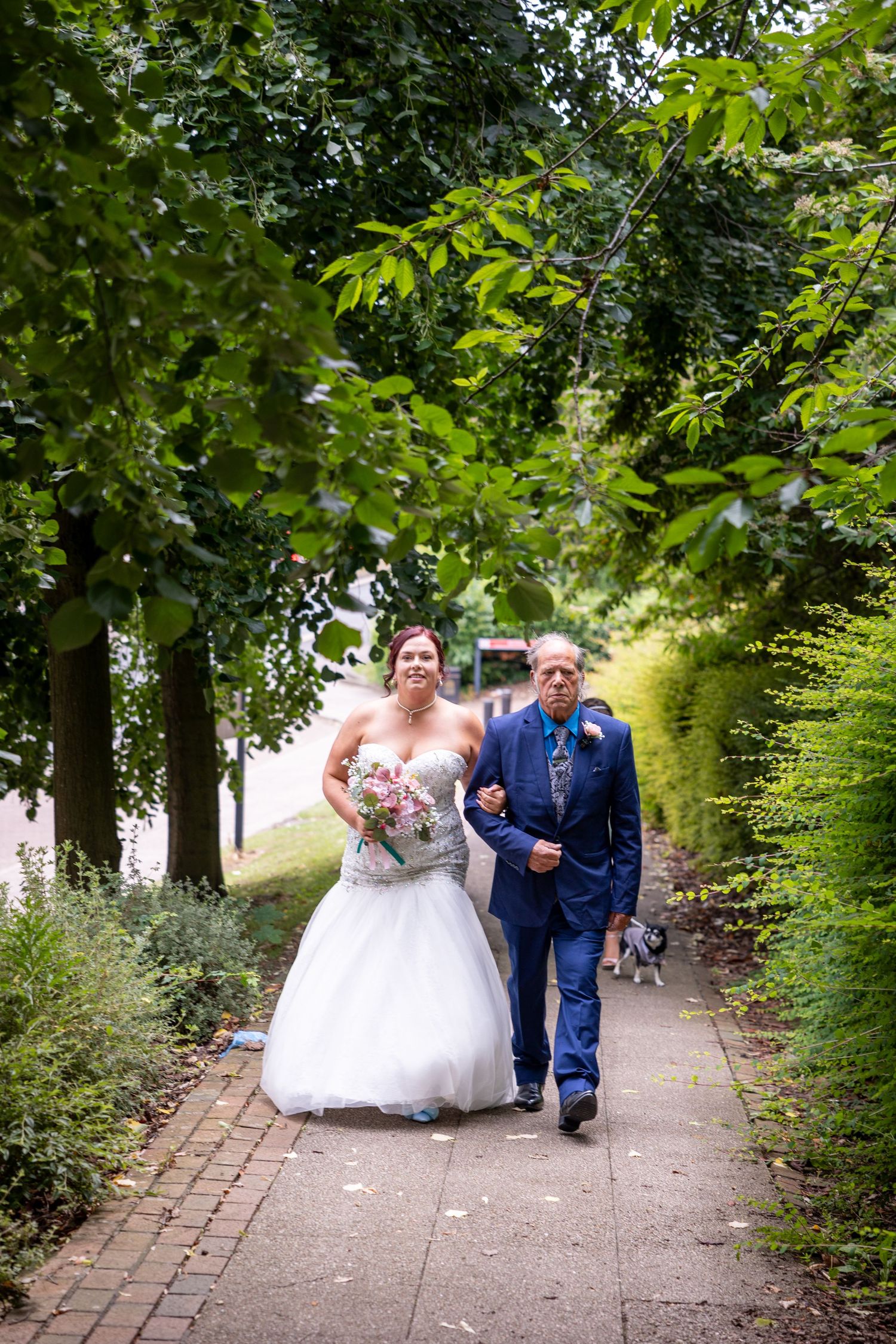 Bride walks with her father along a leafy path in South Shields, a heartfelt wedding moment captured with natural beauty and emotion in the