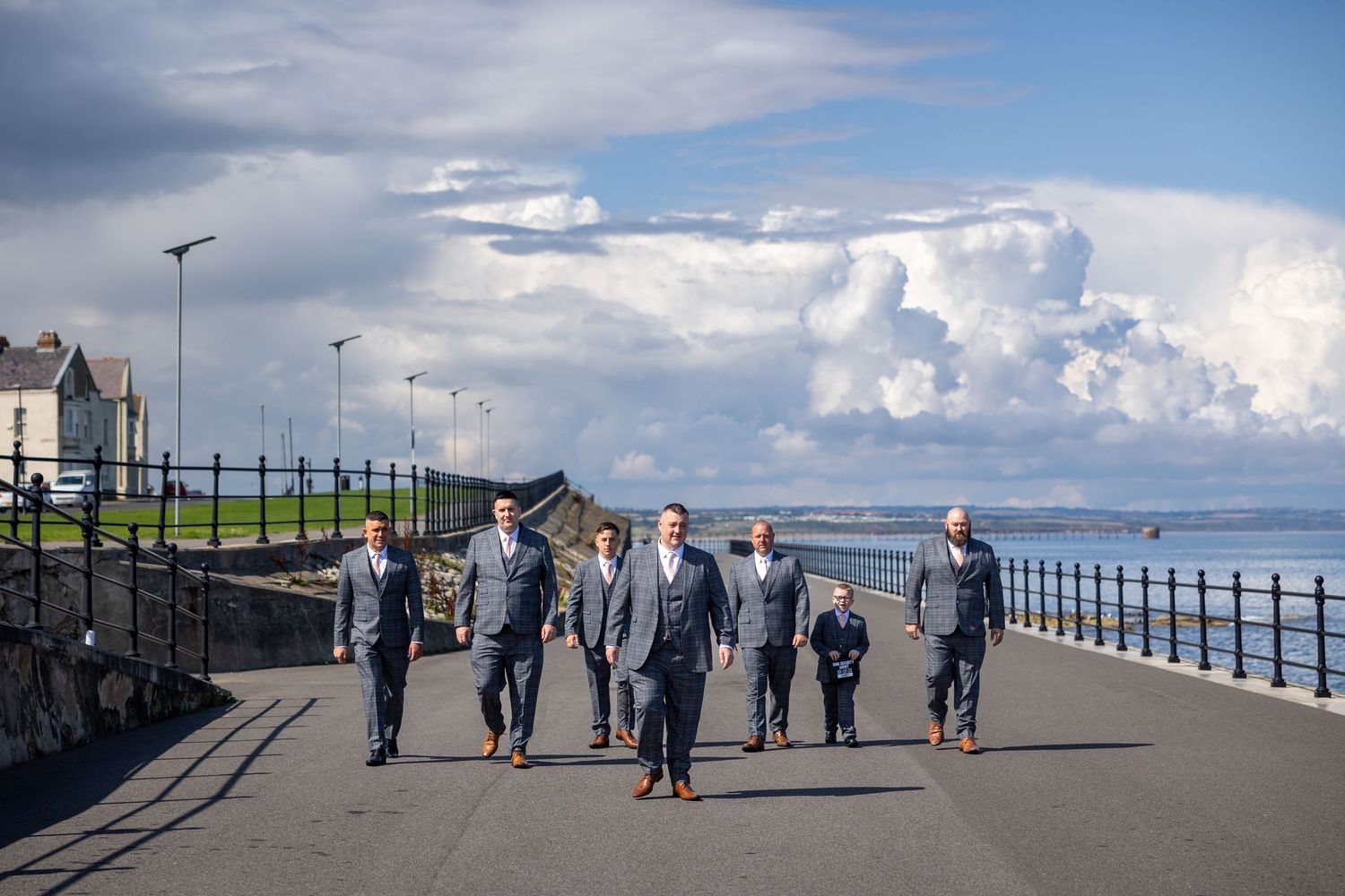 Groom and groomsmen walking along seafront at Hartlepool, dramatic sky, modern documentary wedding photograph