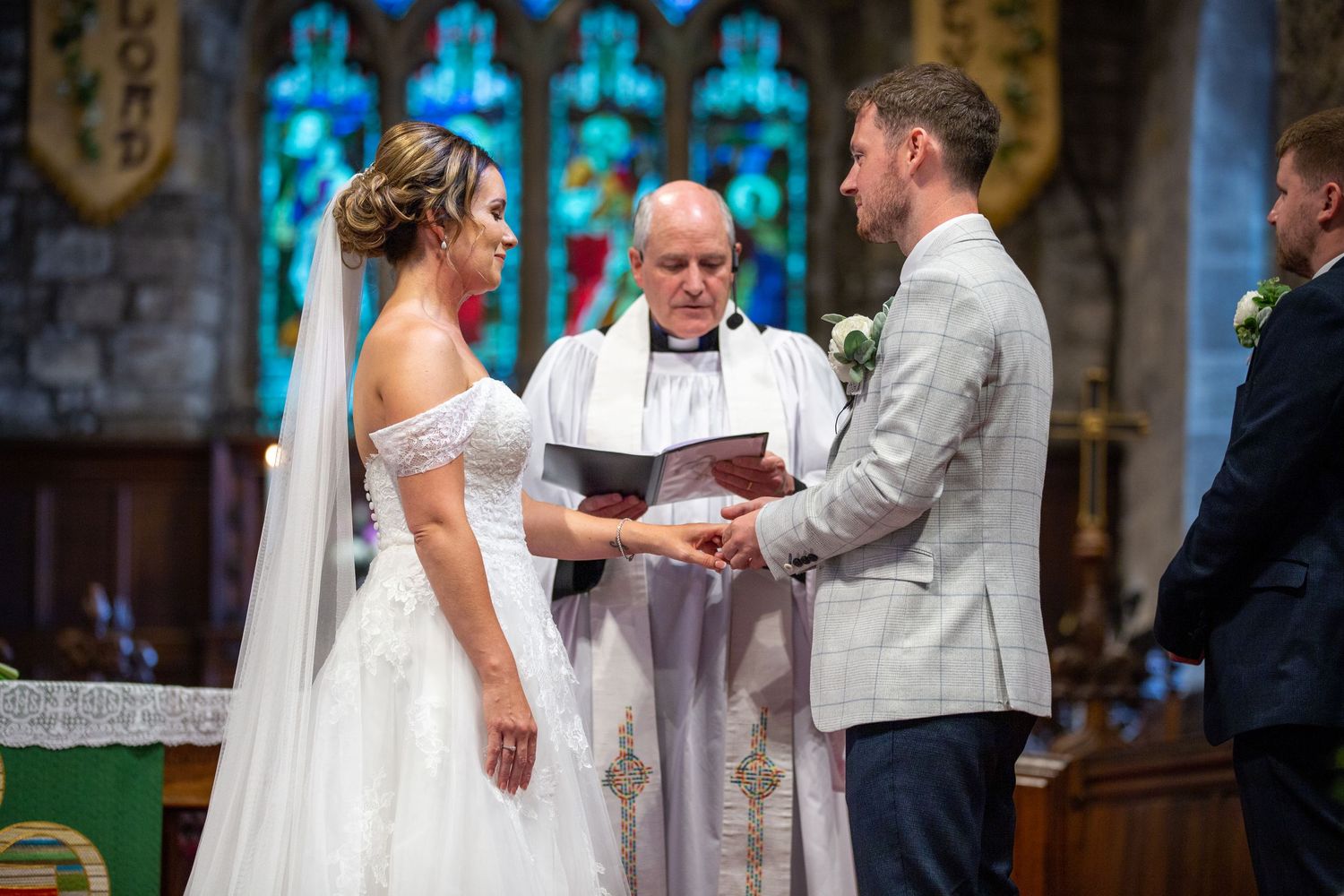 Bride and groom exchanging vows in church, emotional wedding ceremony, ring exchange moment, classic UK wedding with stained glass backdrop